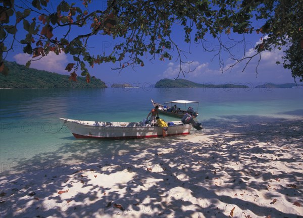 MALAYSIA, Kedah, Langkawi, Pulau Singa Besar wildlife reserve island with men unloading long boats under the shade of the trees