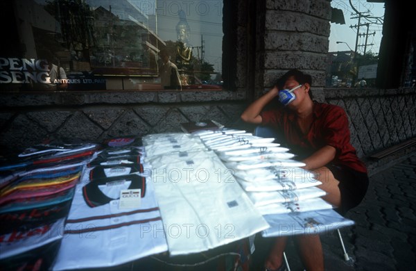 THAILAND, Bangkok, Street shirt vendor asleep beside his stall wearing a smog mask.