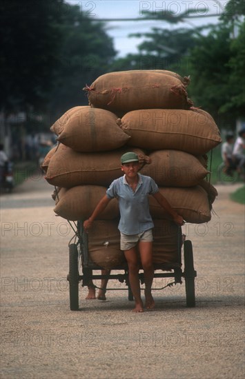 VIETNAM, Transport, Man pulling a loaded cart stacked high with sacks behind him.