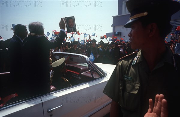 CAMBODIA, Phnom Pehn, Sihanouk and Hun Sen leave Pochentong airport in an open top car past waving crowds and soldiers.