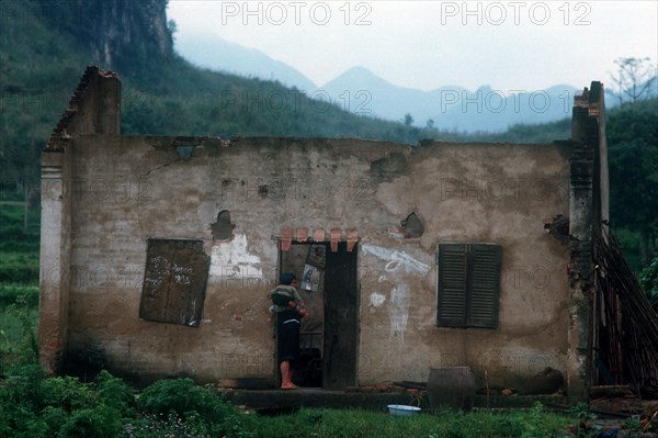 VIETNAM, Lang Son Province, Dong Dang, "Women holding a child, standing in the doorway of the ruined house in which they are living.  China in the distance."