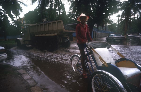 CAMBODIA, Phnom Pehn, Rickshaw and truck driving through a flooded street near the Royal Hotel during Monsoon rains.