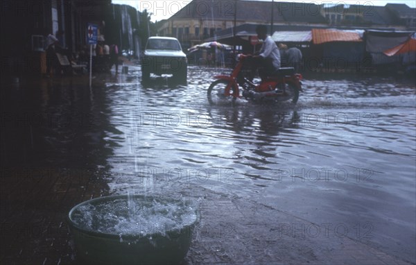 CAMBODIA, Kratie, Motorcyclist driving through a flooded street.