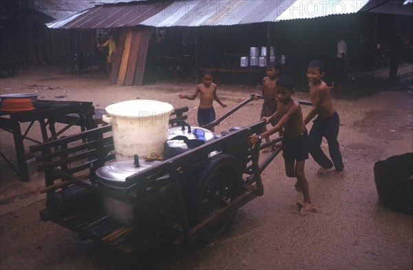 CAMBODIA, Thmar Pouk, A group of young boys pushing a handcart loaded with large containers in heavy rain.