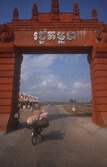 CAMBODIA, Moc Bai, Man on a bicycle crossing the border between Cambodia and Vietnam underneath large archway.