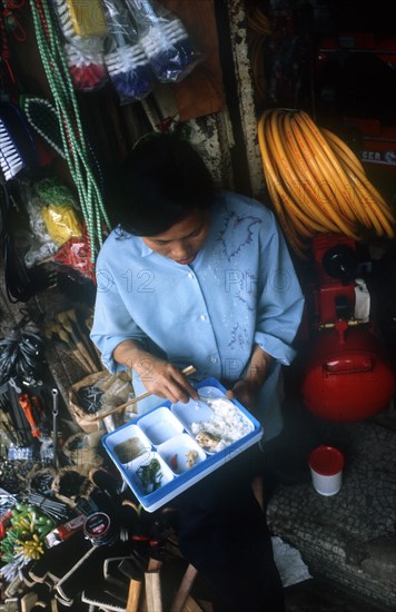 VIETNAM, Ho Chi Minh City, Looking down on a young woman eating from a plastic tray of different dishes in a household goods shop interior.