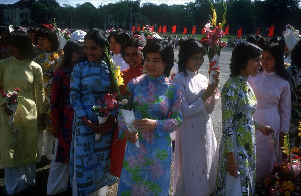 VIETNAM, Hanoi, Young women wearing traditional Cao dai dresses and holding flowers waiting at the finish of a bicycle race.