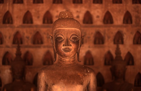 LAOS, Vientianne, Wat Si Saket.  Detail of Buddha figure in the foreground with niches containing more figures behind.