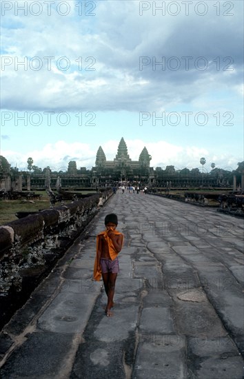 CAMBODIA, Siem Reap, Angkor Wat, Small boy on the stone path leading to the temples which stand against the sky behind.