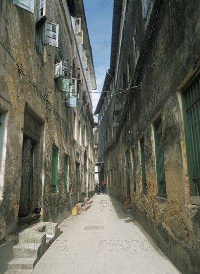 TANZANIA, Zanzibar Island, Zanzibar, "Stone Town.  Quiet, narrow street lined with houses with plaster walls and shuttered windows.  Two women at the far end."
