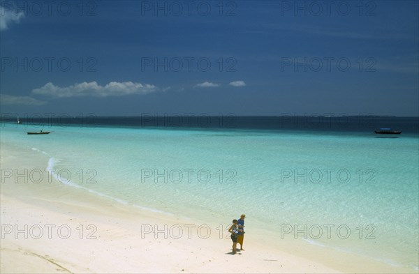 TANZANIA, Zanzibar Island, "Nungwi.  View along beach with white sand and aquamarine sea, towards the skyline.  Couple walking along the shoreline in the foreground. "