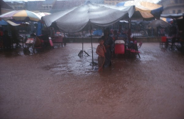 CAMBODIA, Kratie, "People sheltering under large umbrellas during monsoon floods, water covering the ground. "