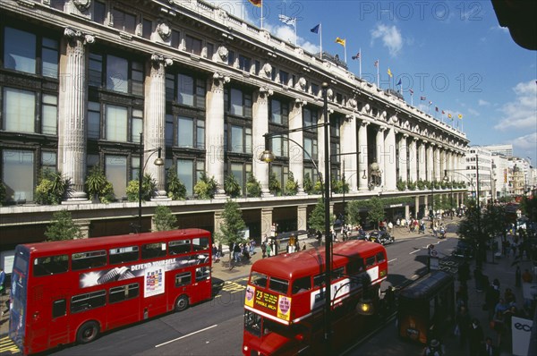 ENGLAND, London, Selfridge’s store exterior with red double decker buses going past on the road in the foreground.Oxford Street