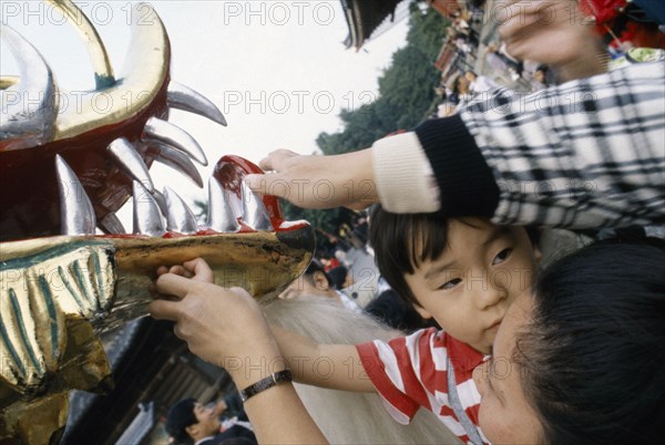 JAPAN, Festival, Young boy held up by his mother to touch the face of the dragon during a dragon dance