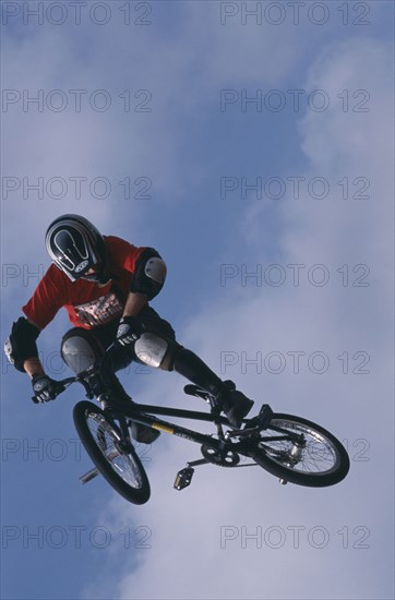 20011105 SPORT Cycling Stunt Bike Cyclist twisting bike in mid air against blue sky and clouds.