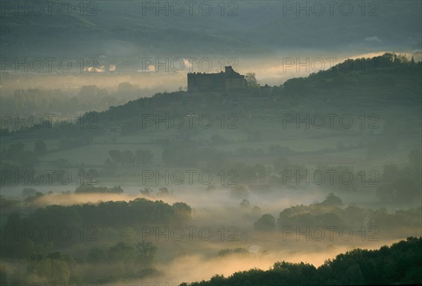 FRANCE, Aquitaine, Dordogne, "Castelnau-Bretenoux Castle silhouetted on hillside against pale, misty sky."