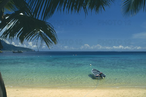 MALAYSIA, East Coast, Pulau Tioman Island, "Panuba Bay, north west coast.  Empty, sandy beach and blue painted boat in shallow water at its edge.  View over sea towards horizon partly framed by palm tree branches. "