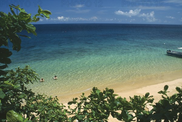 MALAYSIA, East Coast, Pulau Tioman Island, "Panuba Bay, north west coast.  Sandy beach and aquamarine sea with tourist couple bathing.  View partly framed by tree branches. "