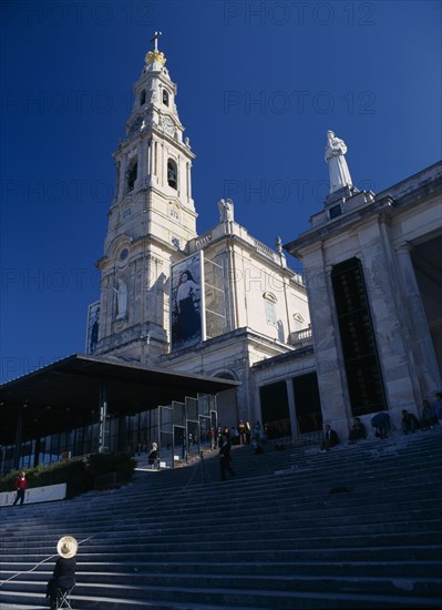 PORTUGAL, Beira Litoral, Fatima, Woman wearing hat seated by steps beneath the church