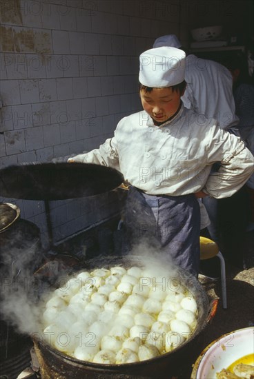 CHINA, Shaanxi Province, Xian, Cook lifting the lid off large dish of frying food.