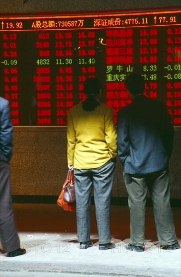 CHINA, Shaanxi Province, Xian, People reading stocks and shares financial information displayed in open fronted roadside building.