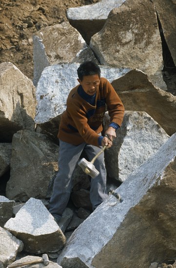 CHINA, Shaanxi Province, Xian, Man splitting rock in a stone quarry using a mallet and metal wedges.