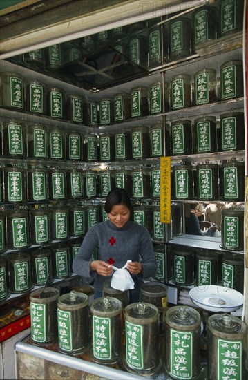 CHINA, Shaanxi Province, Xian, "Young woman serving a customer partly seen reflected in mirrored wall behind her, in a shop selling Chinese medicines stored in jars on surrounding shelves. "