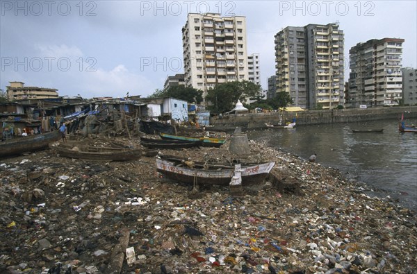 INDIA, Maharashtra, Mumbai , Polluted shoreline covered with rubbish with shanty housing and high-rise buildings behind.