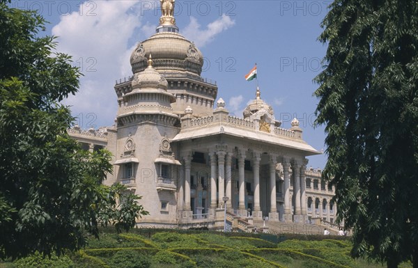 INDIA, Karnataka, Bangalore, "Vidhana Soudha, built in 1954 and housing the Secretariat and the State Legislature.  Exterior with domed roof and steps to colonnaded facade, part framed by trees."