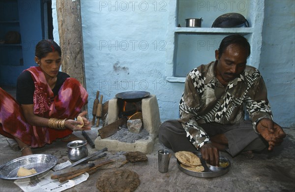 INDIA, Uttar Pradesh, Agra, "Woman cooking chapatis outside over simple, open top stove and serving them to a man sitting on the ground beside her."