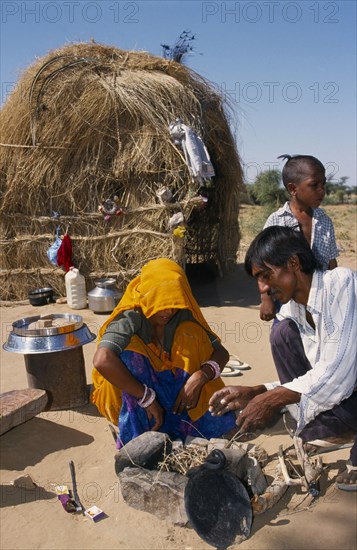 INDIA, Rajasthan, Work, Couple lighting a fire inside stone surround on sandy ground outside their nomadic shelter