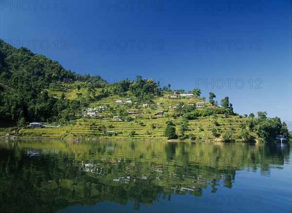 NEPAL, Annapurna Region, Pokhara, View over Lake Phewa with reflected terraced hillside with houses and trees.