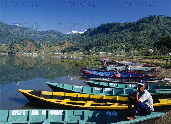 NEPAL, Annapurna Region, Pokhara, Painted wooden rowing boats on Lake Phewa with tree covered hillside behind.