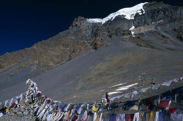 NEPAL, Annapurna Region, Thorung La Pass, Prayer flags hanging at the top of the pass with snow covered mountain peak behind.