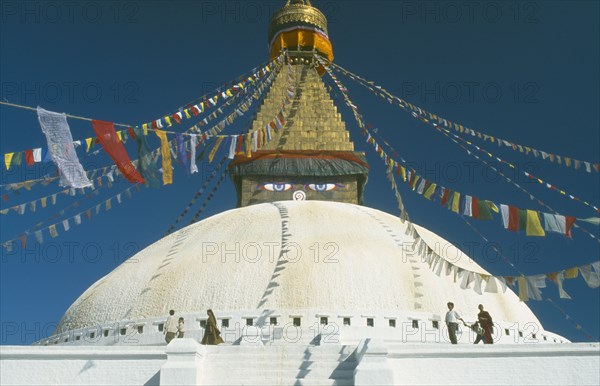 NEPAL, Kathmandu, Bodhnath Stupa, Detail of white dome with visitors circling it clockwise and gilded spire hung with prayer flags and painted eyes at its base.