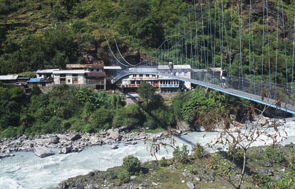 NEPAL, Annapurna Region, Transport, Suspension bridge over fast flowing river near Bhubhule with two trekkers crossing.