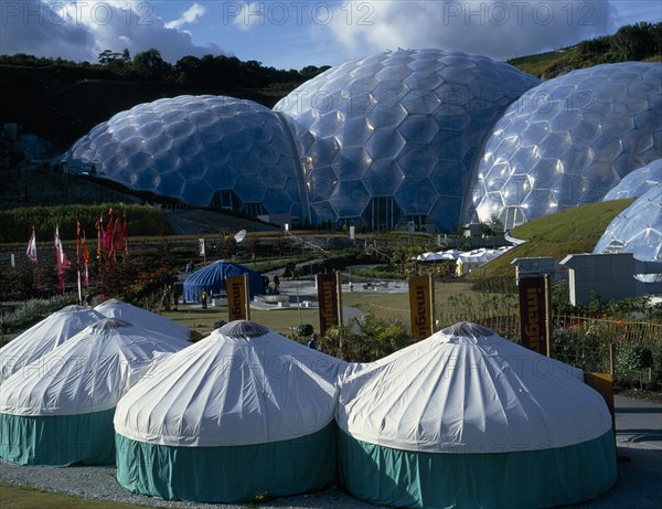 ENGLAND, Cornwall, St. Austell, Eden Project.  General view over the Humid Tropics Biome exterior with green and white yurts in the foreground.