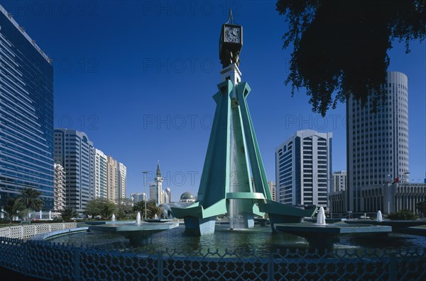 UAE, Abu Dhabi, City centre clock tower with fountain underneath modern structure.  High rise buildings at each side.