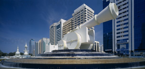 UAE, Abu Dhabi, Al-Ittihad Square with huge sculpture of a cannon set on a circular tiered waterfall with modern high rise buildings behind.