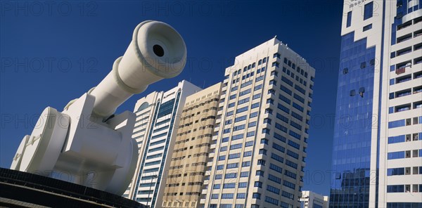 UAE, Abu Dhabi, Al-Ittihad Square.  Angled view of huge sculpture of a cannon with modern high rise buildings behind.