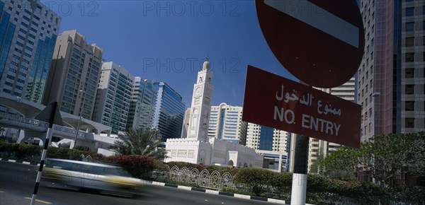 UAE, Abu Dhabi, City centre mosque surrounded by modern high rise buildings with speeding traffic and no entry sign in the foreground.