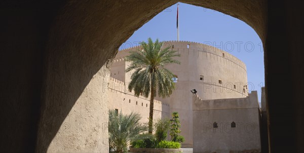 OMAN, Nizwa, "Nizwa Fort, built in the mid seventeenth century.  Exterior view framed by archway in shadow."
