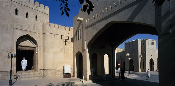 OMAN, Nizwa, Town centre with crenellated walls and archway over quiet street.  Man framed by arched entrance in wall.