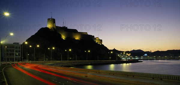 OMAN, Muscat, "Mutrah Fort, built by the Portuguese in the 1580s, situated above town.  Illuminated at night with light trails from traffic on the road below lined by street lights."