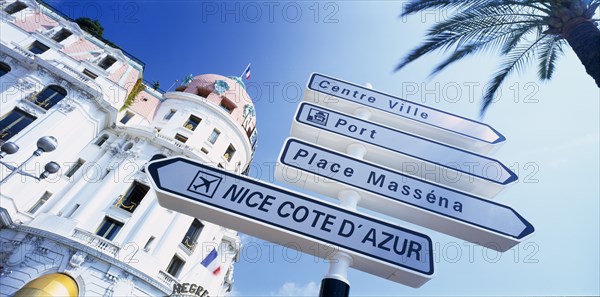 FRANCE, Provence-Cote d’Azur, Nice, "Promenade des Anglais.  Angled view of directional road sign in front of the Hotel Negresco, partly seen behind.  Alpes Maritimes"