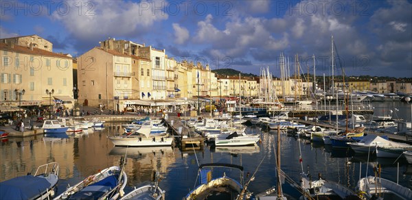 FRANCE, Provence-Cote d’Azur, St Tropez, View over harbour with boats moored beside wooden jetties towards waterside buildings.  Var region..