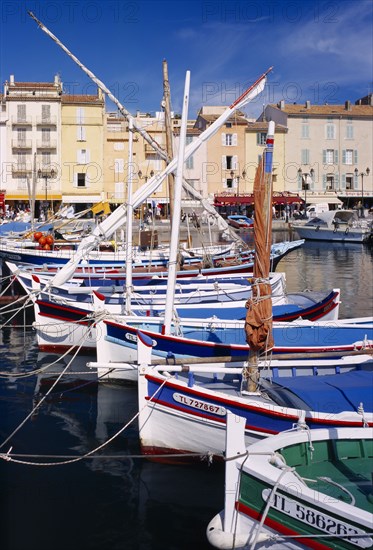 FRANCE, Provence-Cote d’Azur, St Tropez, View along line of moored boats towards waterside buildings.  Var.