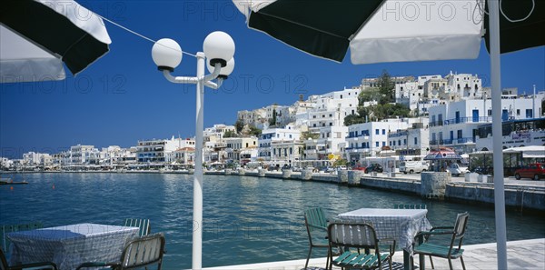 GREECE, Cyclades Islands, Naxos, "Hora. View from waterside eating area under black and white sun umbrellas, towards white painted town buildings."