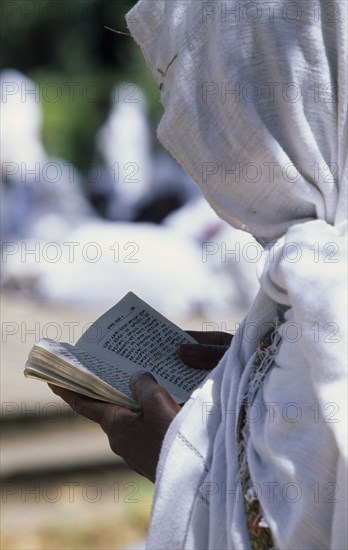 ETHIOPIA, Addis Ababa, "Woman in white head covering reading from book during ceremony at St George Church, Kidus Giorgis."