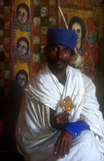 ETHIOPIA, Gonder Province, Gonder, "Church of Debre Birhan Selasie.  Portrait of priest in front of painted wall, holding crucifix. "